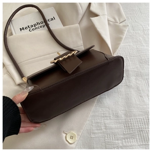 Close-up of brown leather baguette bag with gold chain buckle on a beige blazer