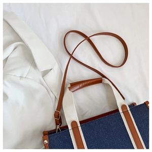 Detail of tote bag showing denim and leather patchwork with adjustable brown shoulder strap