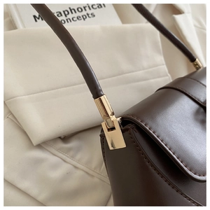 Close-up of golden metal hardware and neat stitching on dark brown leather baguette bag