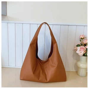 Close-up of a brown synthetic leather tote bag on a beige table next to pink roses