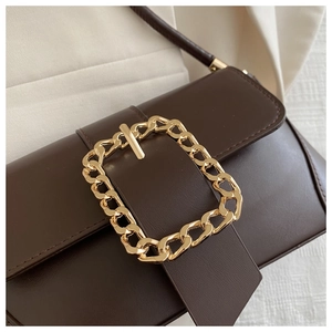 Detail view of deep brown baguette bag with bold gold buckle on soft fabric background