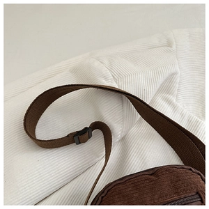 Detail of adjustable canvas strap and brown corduroy texture on minimalist shoulder bag