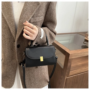 Detail of minimalist black leather crossbody bag featuring a golden rectangular clasp