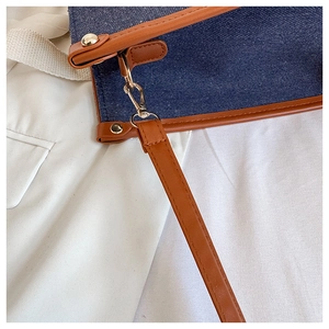 Detail of dark blue denim tote with brown leather trim and golden metal hardware
