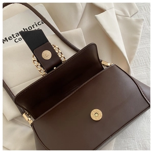 Macro view of dark brown leather handbag with magnetic closure and golden chain detail