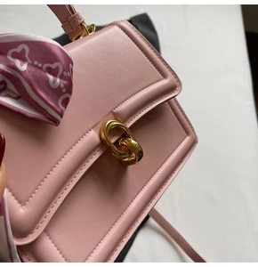 Detail einer rosa Ledertasche mit goldenem Ringverschluss und bedrucktem Seidentuch