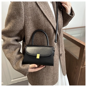 Close-up of black leather crossbody bag with golden buckle on a tweed jacket background
