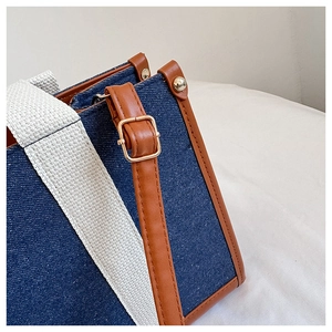 Detail of blue denim tote bag featuring brown leather trim and golden metal hardware