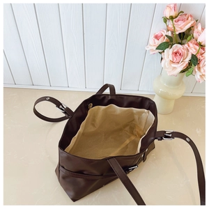 Detail of dark brown tote bag showing beige lining and silver metal buckle adjustment