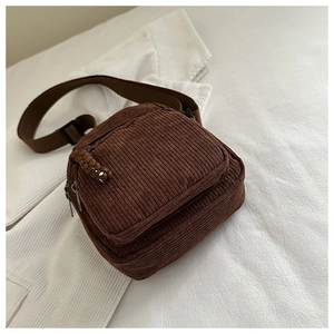 Detailed macro view of the corduroy fabric texture and zipper pocket on a brown crossbody bag