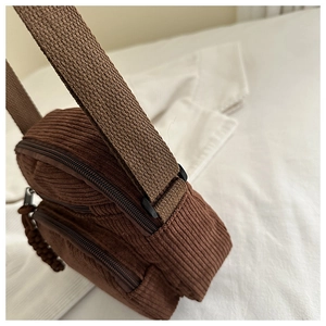 Detailed close-up of brown corduroy crossbody bag texture and multi-layer zippers