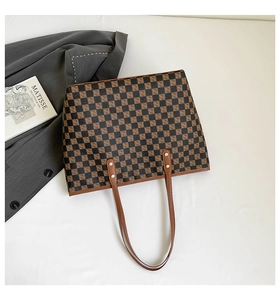 Vista piatta della borsa tote a scacchi marrone con eleganti tracolle lunghe e libro