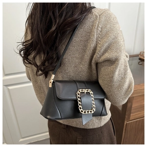 Detail of a vintage black leather baguette bag with a chunky gold chain strap on a model