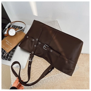 Detail of dark brown leather tote bag with decorative straps on an office desk setting