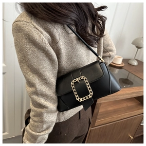 Detail of black baguette bag with gold chain buckle worn over the shoulder