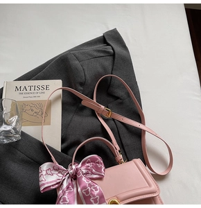 Detaillierte Nahaufnahme der rosa Ledertasche mit Goldschloss und Seidenschal auf Sakko