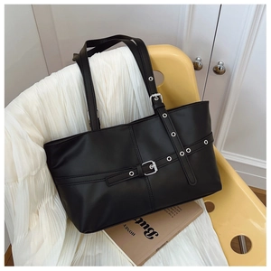 Detail view of black matte leather tote bag with silver metal buckles and eyelet hardware