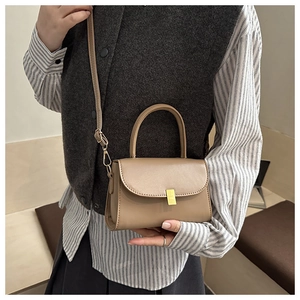 Detail of khaki square handbag with gold metal clasp shown on shoulder with long strap