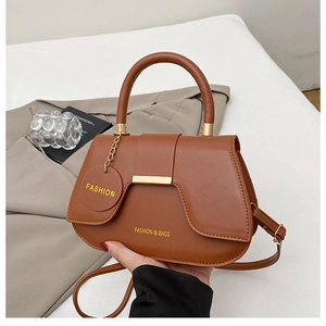 Detail of a brown leather saddle bag featuring a fashion tag and adjustable strap