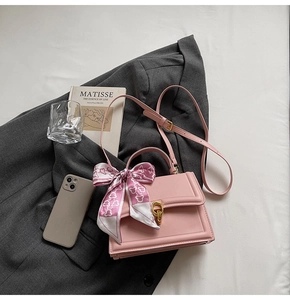 Pink crossbody bag with gold buckle and silk scarf detail styled on a dark blazer