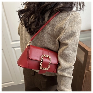 Detail of red baguette shoulder bag featuring a gold chain buckle and smooth leather finish