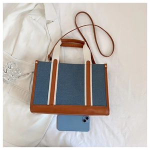 Detail of blue denim canvas tote bag with brown faux leather trim and long strap