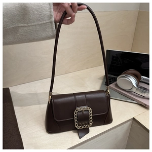 Close-up of a dark brown baguette bag with a large gold chain buckle on a minimalist desk