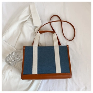 Detail of blue denim tote bag featuring brown faux leather trim and cream woven handles