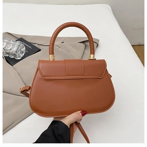 Chic brown saddle bag with gold hardware shown in a lifestyle scene with blazer and books