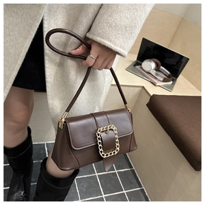 Detail of a brown baguette bag with a decorative gold chain buckle and stitching