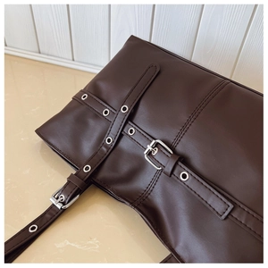 Close-up of brown leather tote bag with silver metal eyelets and decorative straps