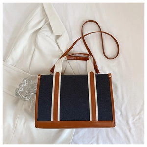 Close-up of black denim tote bag with brown leather trim and golden metal rivet details
