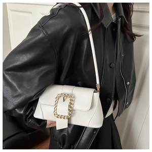 Detail of white baguette shoulder bag with gold chain buckle worn over a black leather jacket