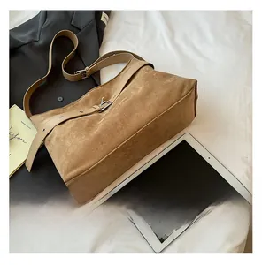 Vue détaillée d'un sac cabas en daim marron avec bandoulière réglable en cuir sur literie blanche