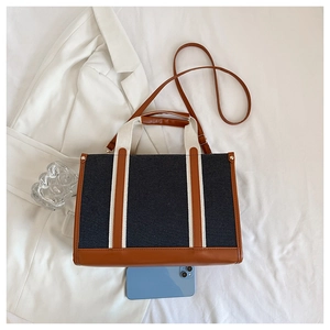 Detail of navy canvas tote bag with brown leather trim and smartphone for size reference