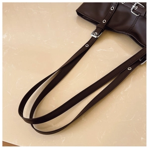 Detailed close-up of dark brown leather tote strap with silver metal eyelets and buckle