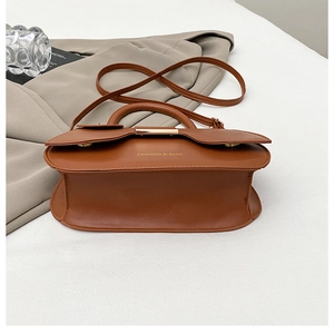 Detailed view of brown leather saddle bag with fashion text and metallic clasp buckle