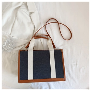Detail of a denim tote bag with brown leather trim and white straps in a lifestyle setting