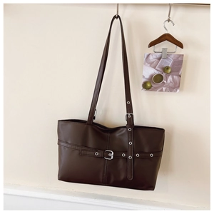 Detail of dark brown tote bag with decorative straps and metal buckles on a white wall