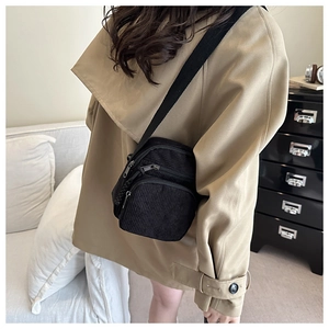 Detailed view of black corduroy crossbody bag with zippers worn over a beige coat