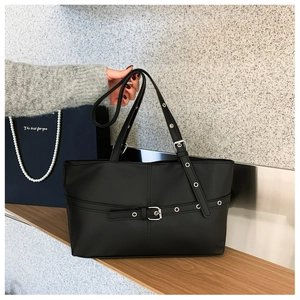 Detailed view of a black tote bag with buckle straps and a gift bag background