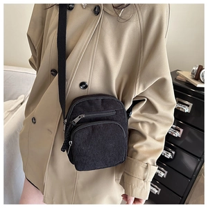 Vertical black corduroy crossbody bag with dual zipper pockets on a stylish model