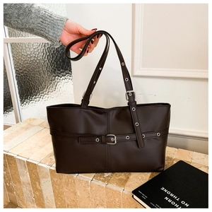 Detail of dark brown tote bag featuring decorative straps with metallic eyelets and buckles