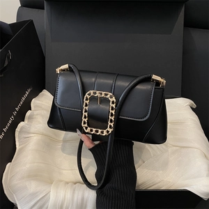 Minimalist black leather baguette bag with gold chain buckle held against gift boxes