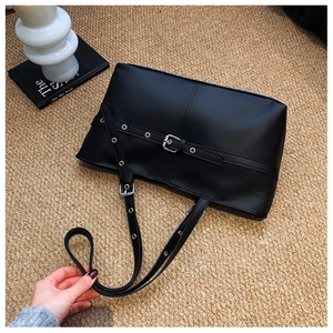 Detail view of black PU leather shoulder bag with punk-style eyelet buckles and straps