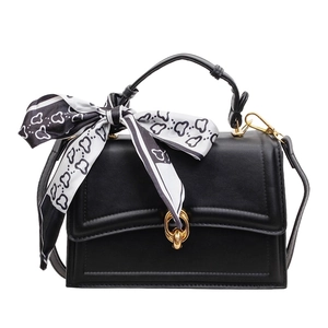 Minimalist black leather handbag with a gold ring buckle and decorative silk scarf