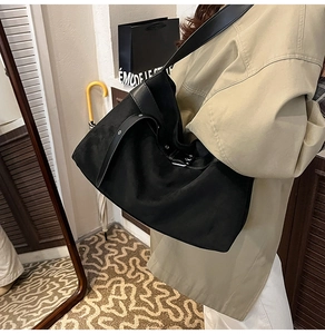 Détail d'un grand sac cabas noir en daim avec bandoulière en cuir porté par un mannequin