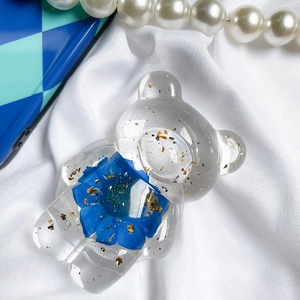 Detail of transparent bear phone grip with blue dried flowers and gold leaf foil