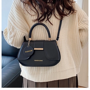 Detail of black saddle bag with gold metal trim and fashion pendant on a knit sweater