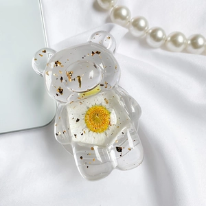 Detail of bear shaped phone grip featuring embedded white daisy and gold foil accents